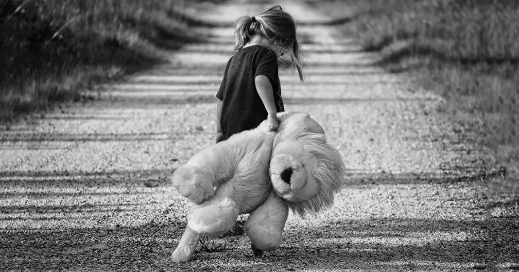 Foto de uma criança triste por problemas no círculo familiar, de costas carregando um urso de pulucia