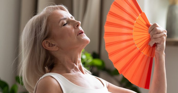 Stressed old woman waving fan suffer from overheating at home